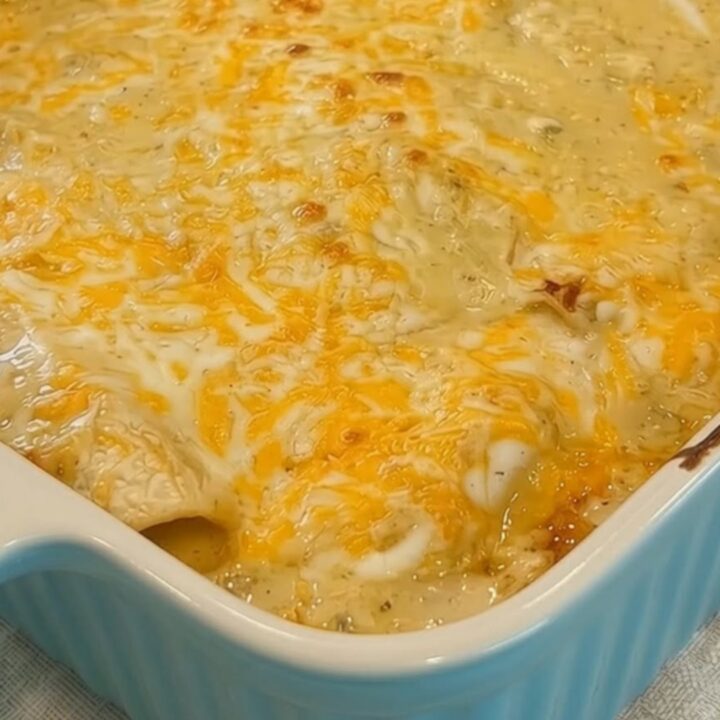 A spatula lifting a creamy white chicken enchilada from a light blue baking dish with a long cheese pull.