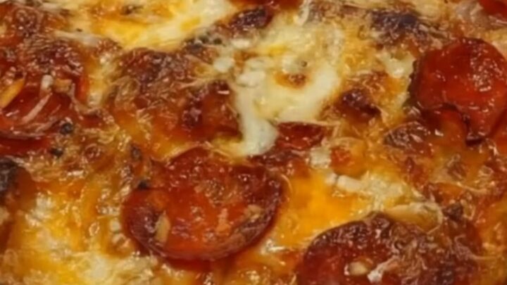A close-up view of a serving spatula lifting a portion of hot, cheesy pizza casserole from a glass baking dish.