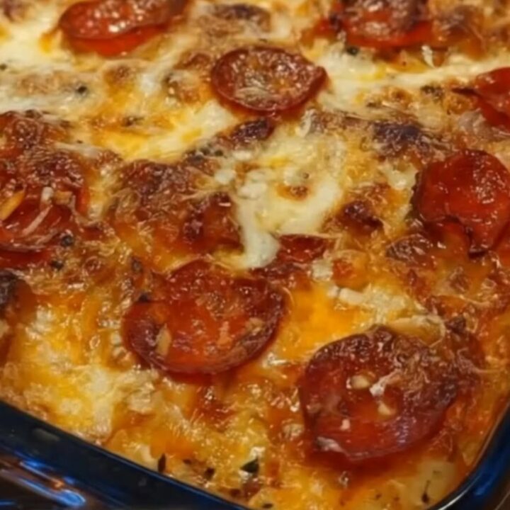 A close-up view of a serving spatula lifting a portion of hot, cheesy pizza casserole from a glass baking dish.