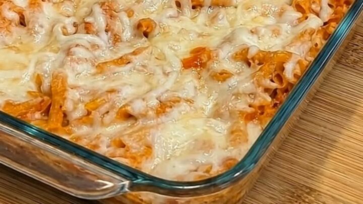 A serving spoon scooping into a golden-brown chicken parmesan casserole, pulling up long