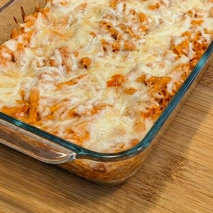 A serving spoon scooping into a golden-brown chicken parmesan casserole, pulling up long