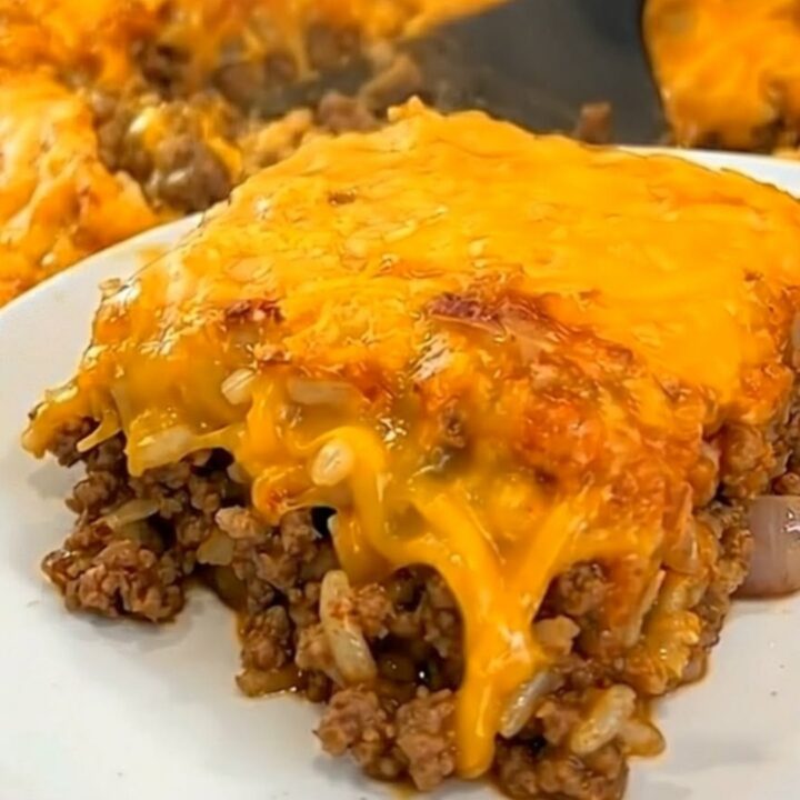 A square portion of Tex-Mex beef and cauliflower casserole on a white plate with melted golden cheese.
