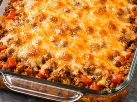 A rectangular glass baking dish filled with savory beef taco casserole and bubbly melted cheese on a gray marble surface