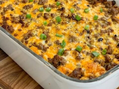 Une casserole de petit-déjeuner dorée et fondante dans un plat en céramique blanc sur une planche en bois.