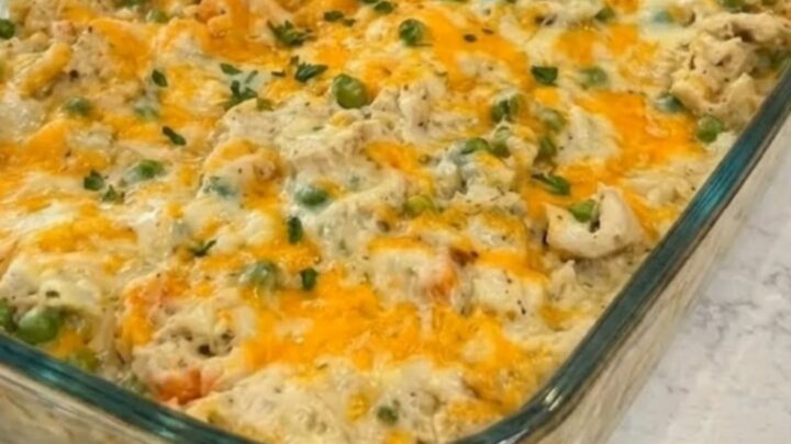 A steaming portion of cheesy chicken and rice casserole being lifted from a glass baking dish with a spoon.