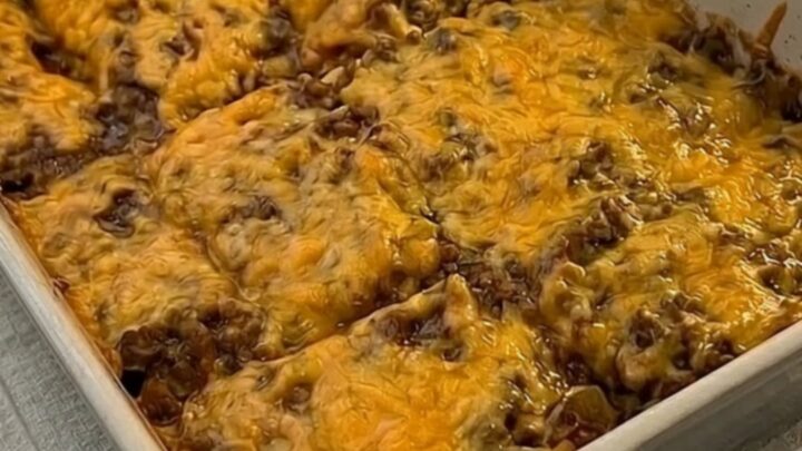 A golden, bubbly cheesy burrito bake in a grey ceramic pan with steam rising from a portion being lifted by a spatula.