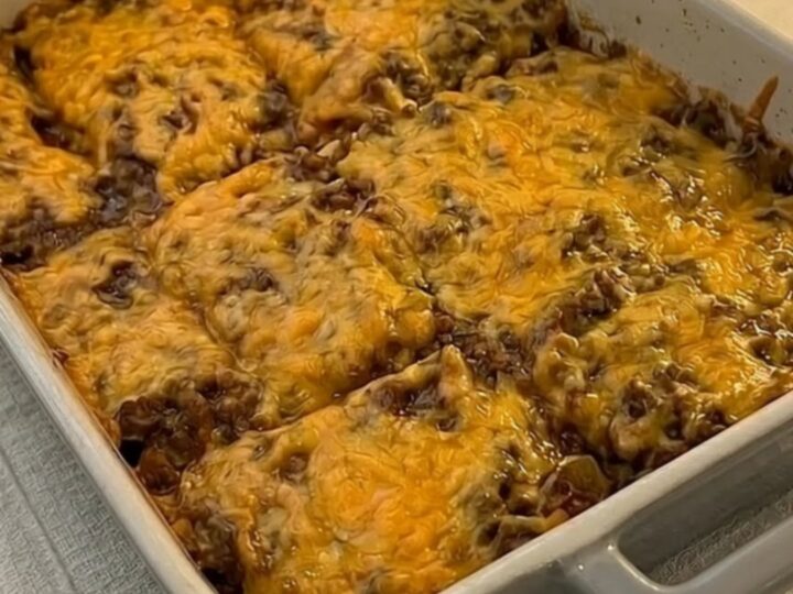 A golden, bubbly cheesy burrito bake in a grey ceramic pan with steam rising from a portion being lifted by a spatula.