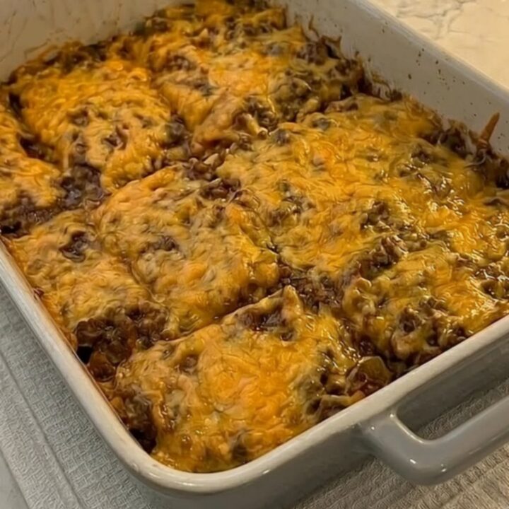 A golden, bubbly cheesy burrito bake in a grey ceramic pan with steam rising from a portion being lifted by a spatula.