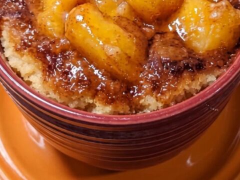 A warm peach cobbler mug cake in a dark red mug sitting on an orange saucer.