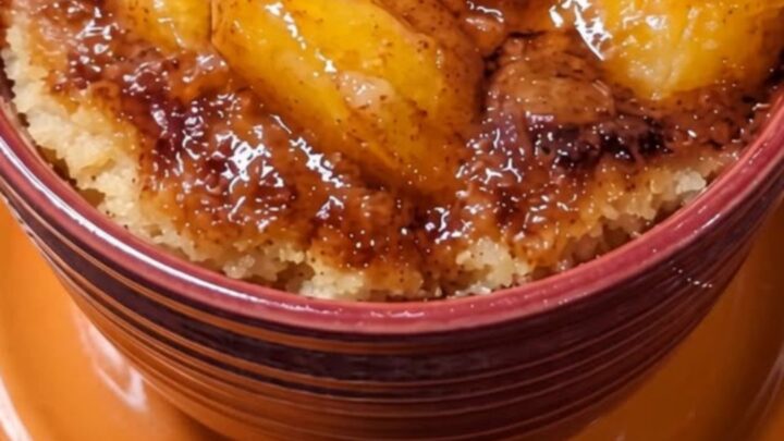 A warm peach cobbler mug cake in a dark red mug sitting on an orange saucer.