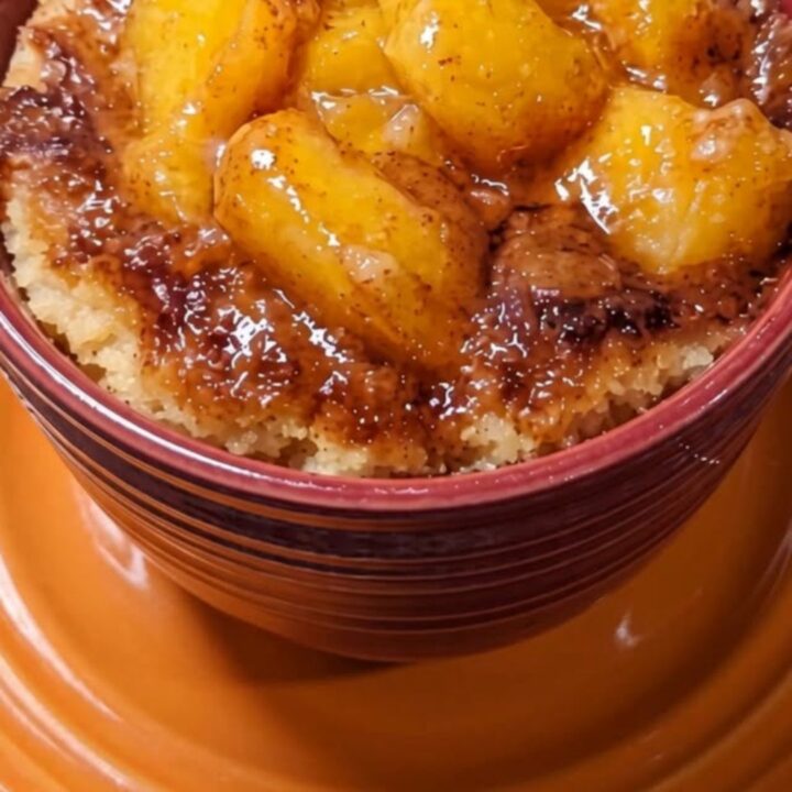 A warm peach cobbler mug cake in a dark red mug sitting on an orange saucer.
