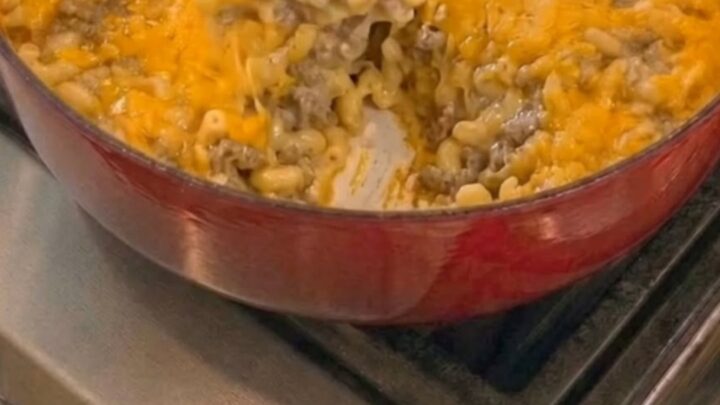 A wooden spoon scooping gooey, melted cheddar and elbow macaroni from a red enameled Dutch oven.