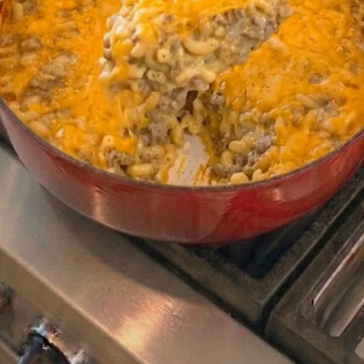 A wooden spoon scooping gooey, melted cheddar and elbow macaroni from a red enameled Dutch oven.