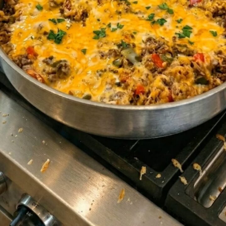 A stainless steel skillet on a gas stovetop filled with seasoned ground beef, rice, and peppers