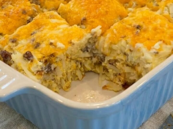 A steaming golden-brown cheesy sausage hash brown breakfast casserole in a pale blue fluted baking dish.