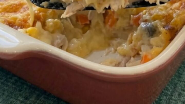 A warm baking dish filled with golden-brown chicken cobbler, with a spatula lifting a cheesy scoop of chicken and peas.