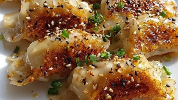 A white platter lined with perfectly crispy pan-fried gyoza dumplings garnished with toasted sesame seeds and green scallions
