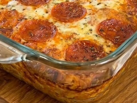 A square slice of warm pepperoni pizza bake being lifted from a glass dish with an epic mozzarella cheese pull.