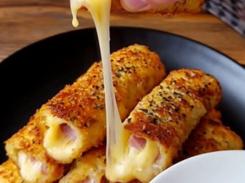 Roulés dorés au jambon et mozzarella fondante empilés sur une assiette sombre.