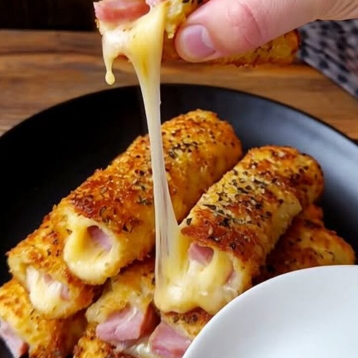 Roulés dorés au jambon et mozzarella fondante empilés sur une assiette sombre.
