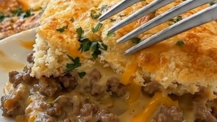 A steaming ground beef cobbler in a baking dish with a golden, fluffy biscuit topping and melted cheddar cheese.