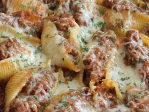 A cast iron skillet filled with jumbo stuffed shells covered in melted, bubbling mozzarella and garnished with fresh parsley.