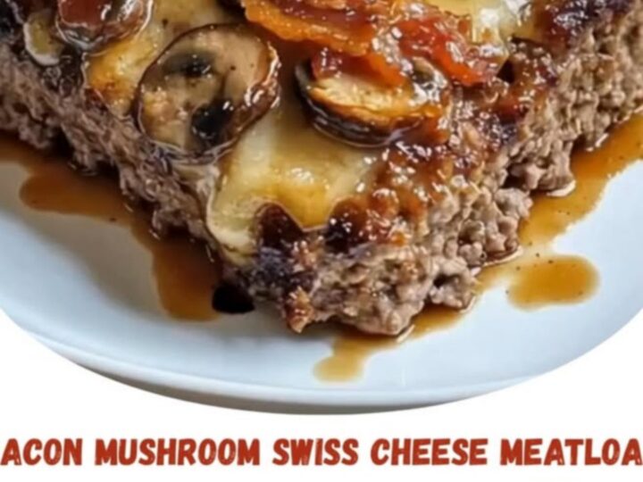 A rectangular meatloaf topped with melted Swiss cheese, sautéed mushrooms, bacon, and fresh thyme on a white plate.