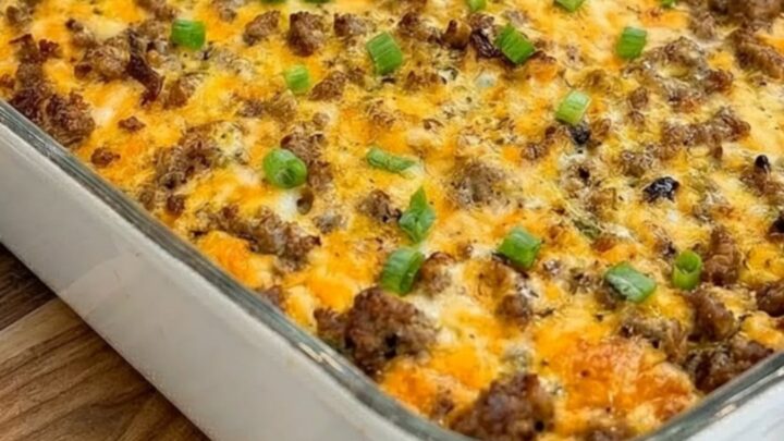A golden-brown baked sausage and hash brown breakfast casserole in a white dish on a wooden board