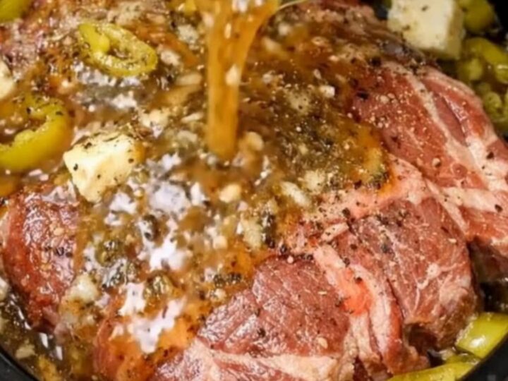 A glossy slow cooker pepperoncini pot roast shredded and surrounded by tangy peppers in a black slow cooker