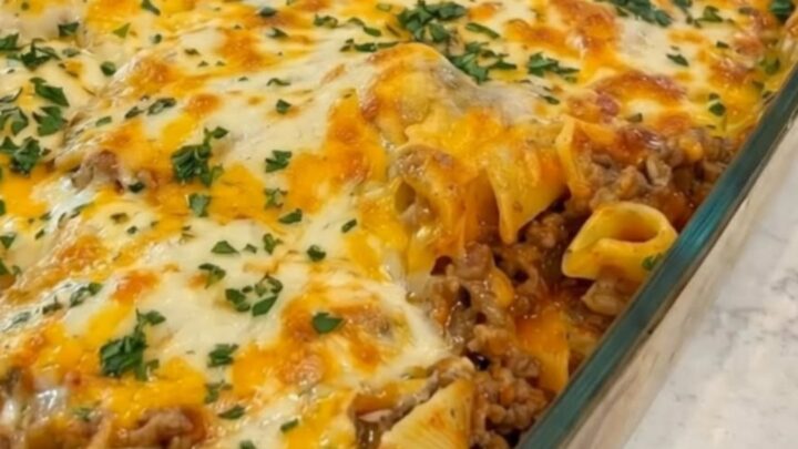 A baked glass casserole dish filled with bubbling browned cheese and fresh chopped parsley on a marble counter