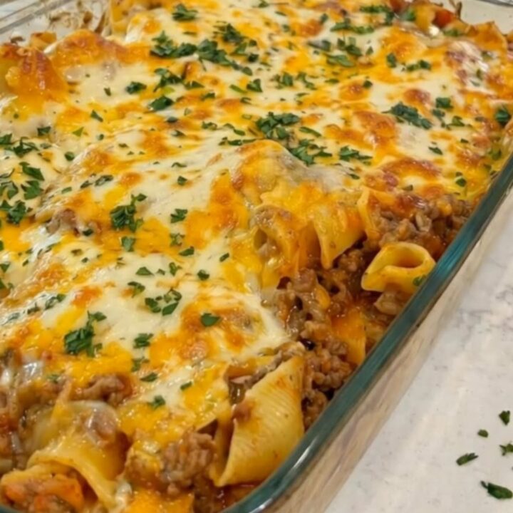 A baked glass casserole dish filled with bubbling browned cheese and fresh chopped parsley on a marble counter