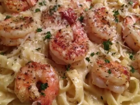 A close-up of creamy fettuccine Alfredo with seared pink shrimp in a skillet.