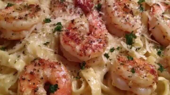 A close-up of creamy fettuccine Alfredo with seared pink shrimp in a skillet.