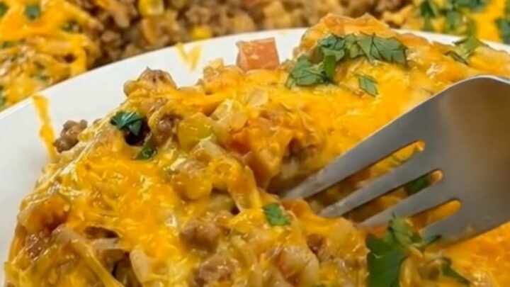 A close-up of a fork lifting a portion of hot taco rice casserole, stretching melted cheddar cheese upward.