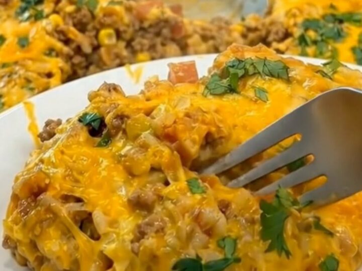 A close-up of a fork lifting a portion of hot taco rice casserole, stretching melted cheddar cheese upward.