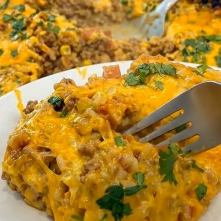 A close-up of a fork lifting a portion of hot taco rice casserole, stretching melted cheddar cheese upward.