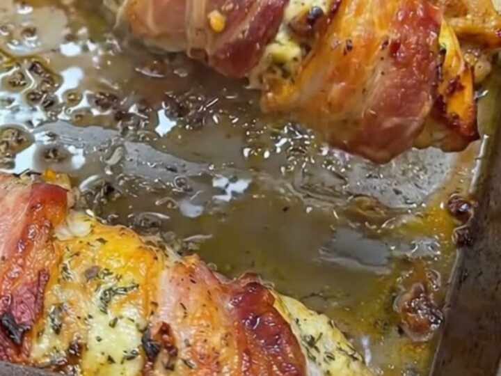 A golden, bacon-wrapped stuffed chicken breast on a plate with fresh herbs.