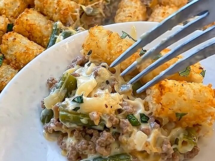 A golden, bubbling green bean tater tot casserole in a glass baking dish with a plated portion in the foreground.