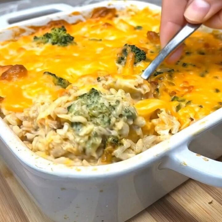 A steaming chicken broccoli rice casserole in a white ceramic dish with a bubbly, golden-brown cheddar crust.