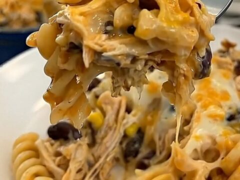 A cheesy bite of fiesta chicken casserole lifted on a fork, showing long glossy melted cheese strings.