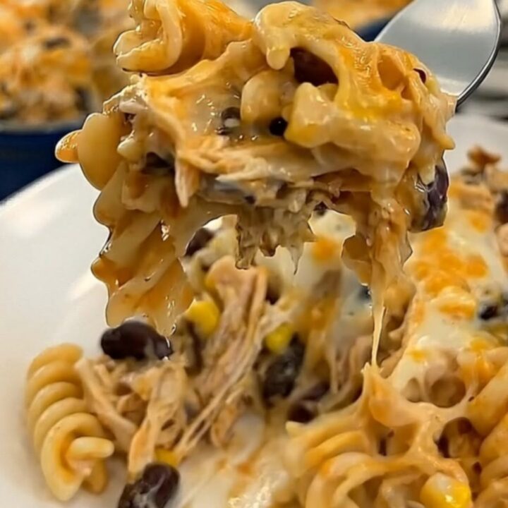 A cheesy bite of fiesta chicken casserole lifted on a fork, showing long glossy melted cheese strings.