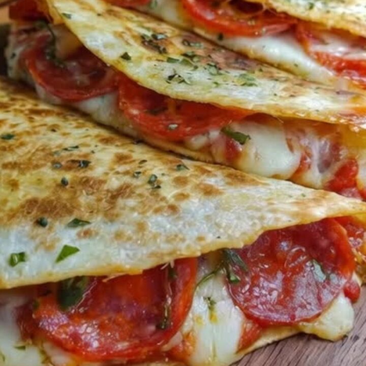 Three crispy pepperoni pizza quesadillas arranged on a wooden board with fresh herbs.