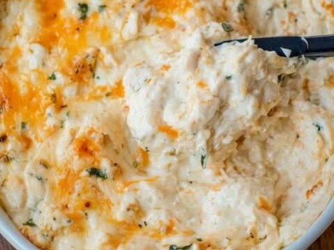 Plat de dip chaud au crabe et cheddar doré, servi avec des crackers sur une planche en bois.