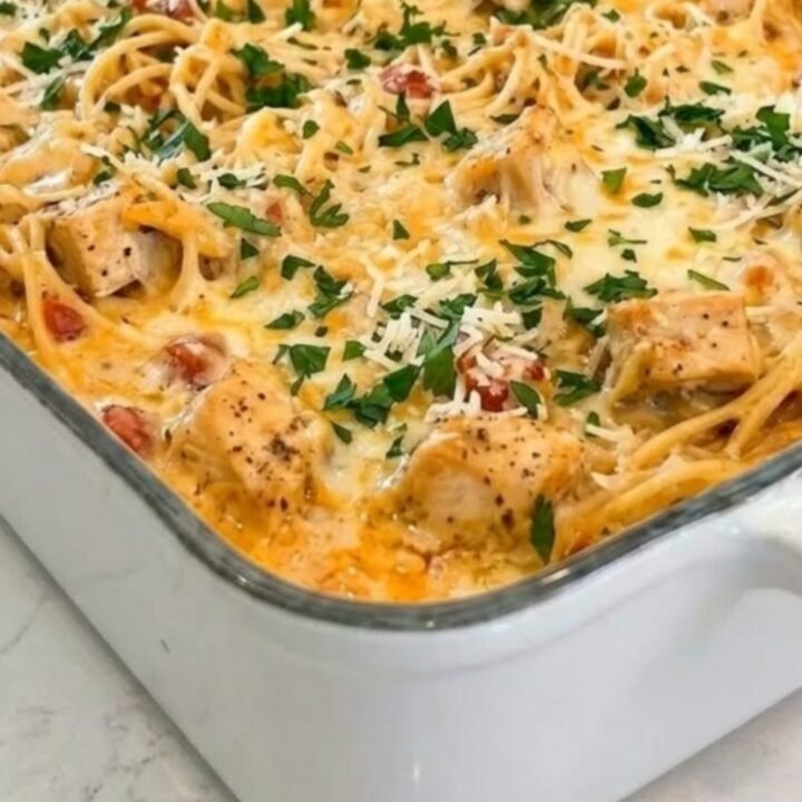 A white rectangular baking dish filled with cheesy baked chicken spaghetti on a bright kitchen counter.