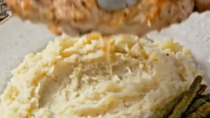 A juicy herb-seasoned chicken breast served on a bed of fluffy mashed potatoes with garlic butter drizzled over.