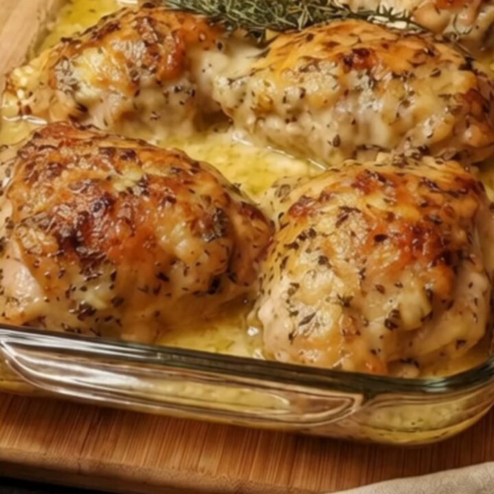 Six golden herb-crusted chicken thighs baked in a rectangular glass dish with bubbling creamy sauce and fresh thyme.
