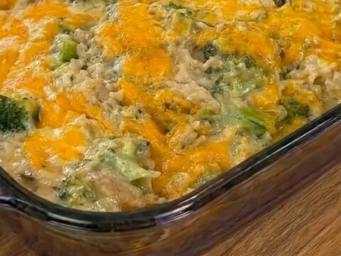 A steaming scoop of cheesy chicken broccoli rice casserole being lifted from a glass baking dish with a long cheese pull.