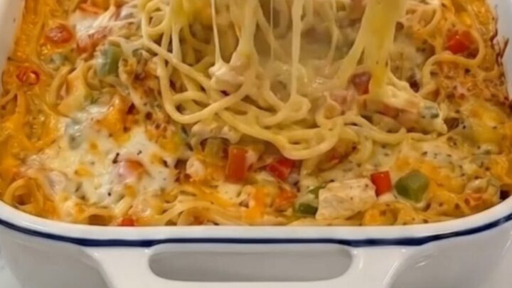 A piping hot, bubbly chicken spaghetti casserole fresh from the oven, served in a blue-rimmed white baking dish.