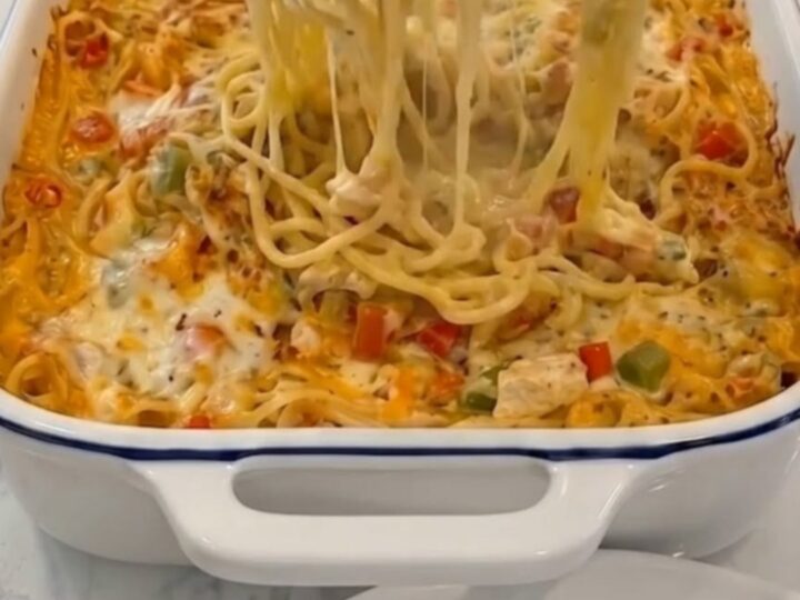 A piping hot, bubbly chicken spaghetti casserole fresh from the oven, served in a blue-rimmed white baking dish.