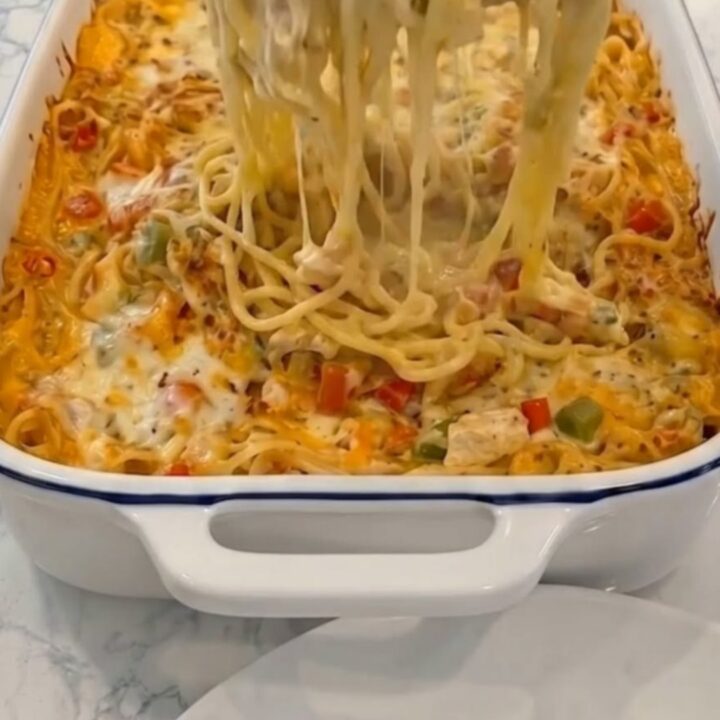 A piping hot, bubbly chicken spaghetti casserole fresh from the oven, served in a blue-rimmed white baking dish.